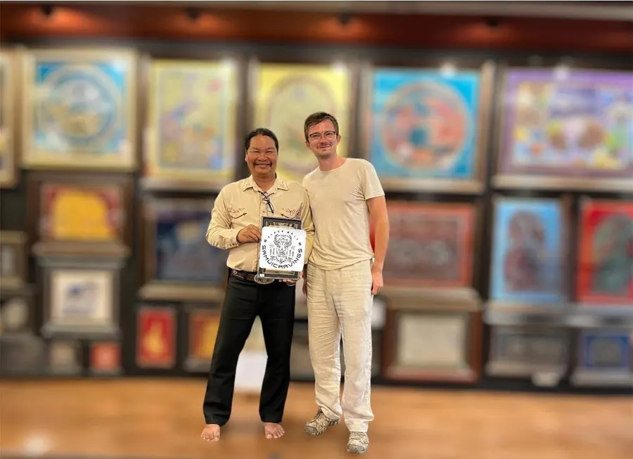 The artist with a guest holding a small framed leather carving in his gallery