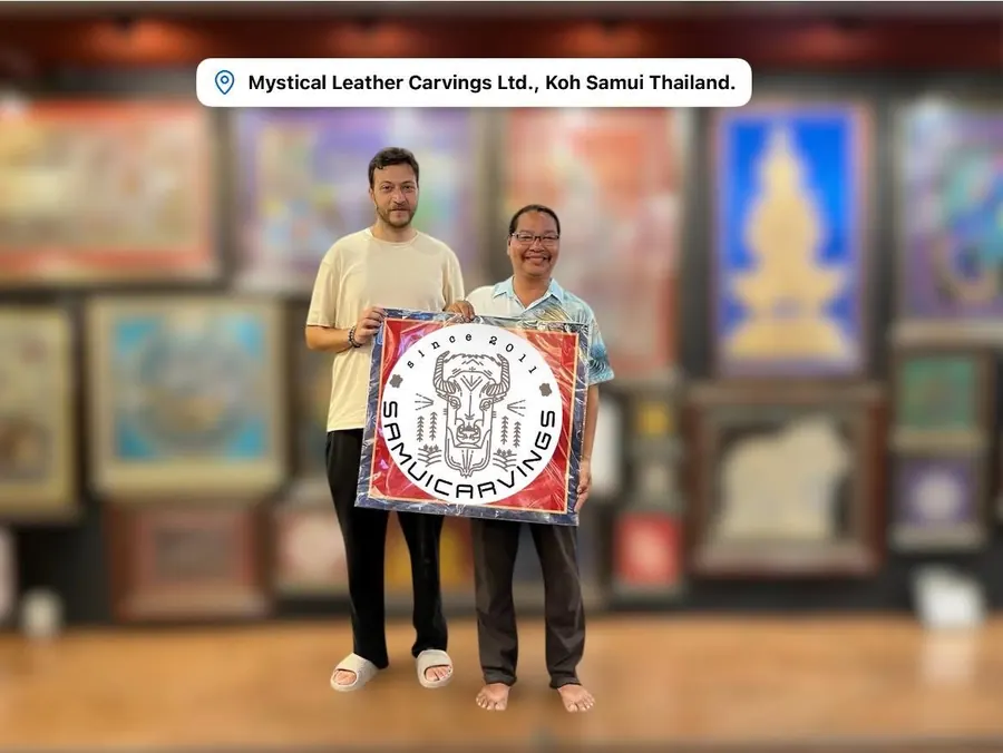 The artist with a guest holding a leather carving in a red wrap, in his gallery