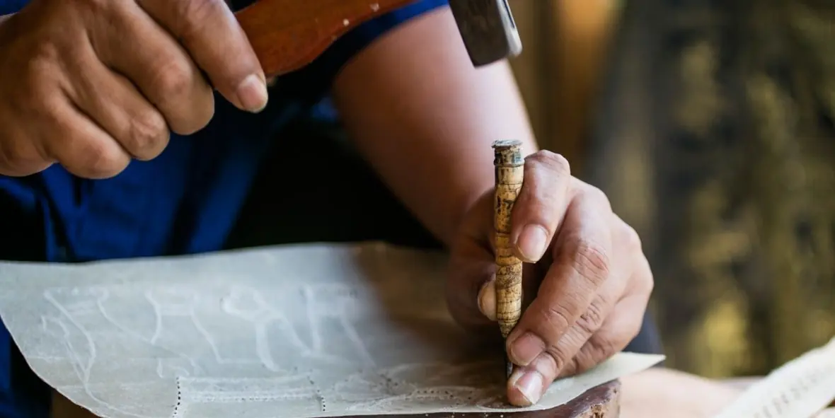 Hands punching an outline into raw hide with a hammer and punch