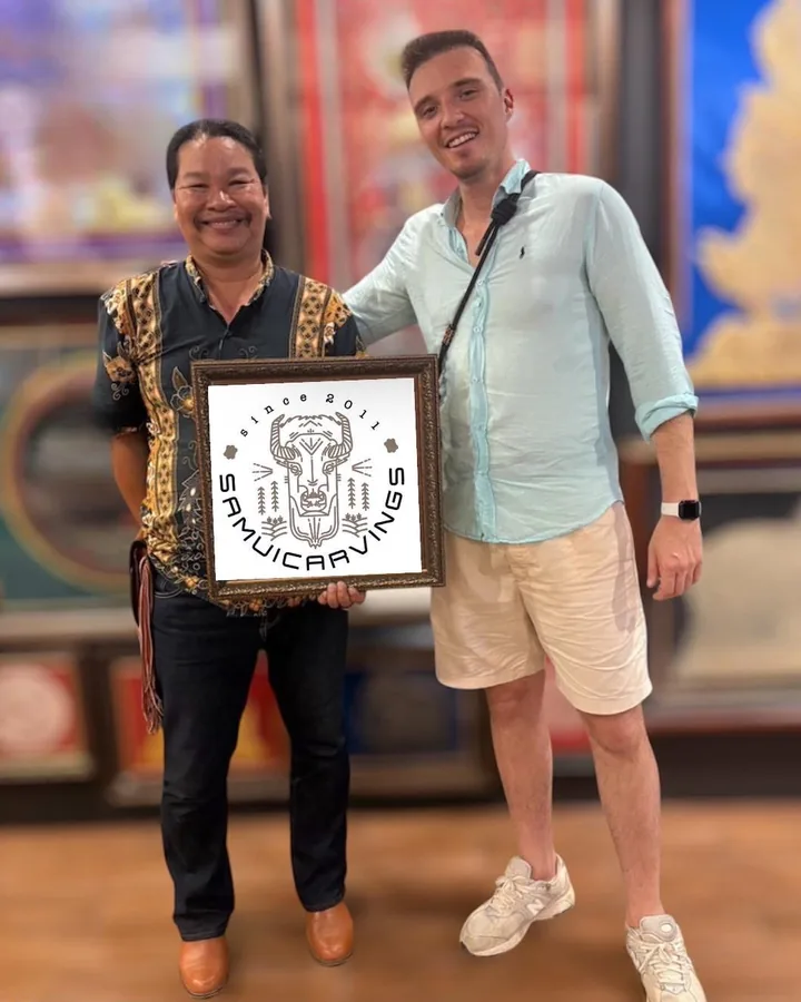 Mr. Choawalit and a guest in the gallery, holding a framed Samui Carvings print